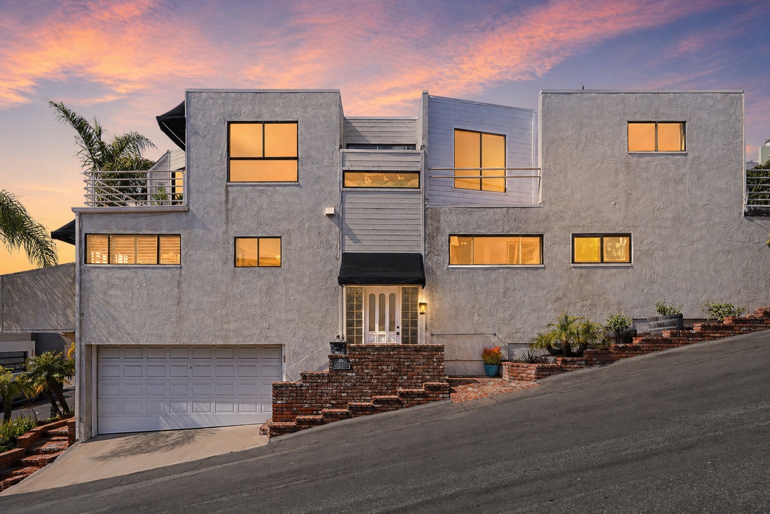 Multi-level modern white home with black awnings on a hillside in Laguna Beach